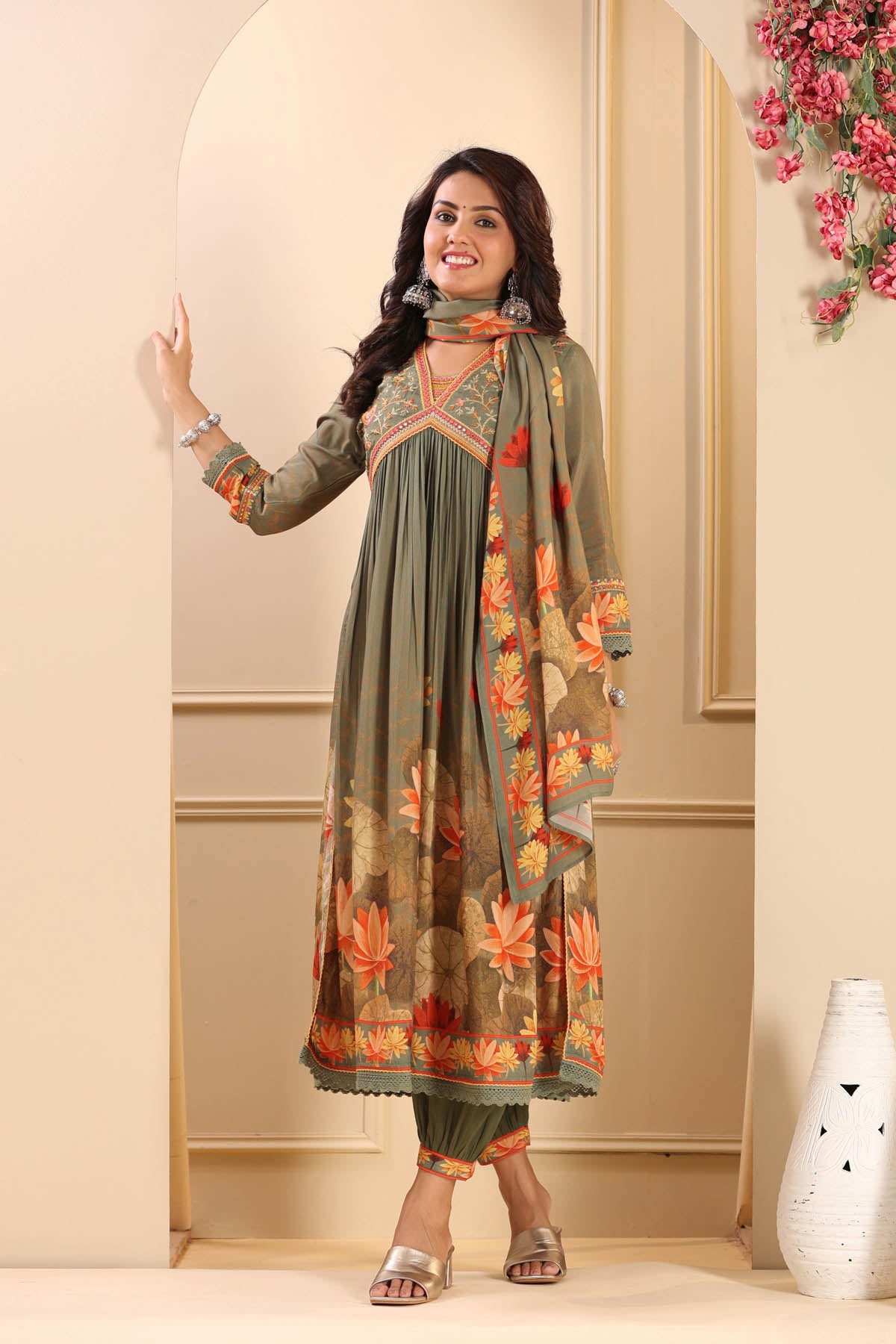 Woman wearing a traditional outfit with a floral dupatta in a decorated room.