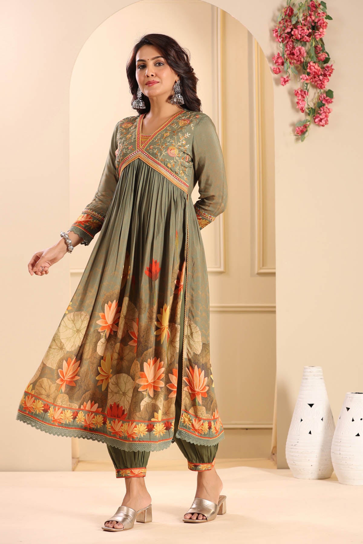 Woman wearing a green and orange traditional outfit with floral patterns in a decorated room.