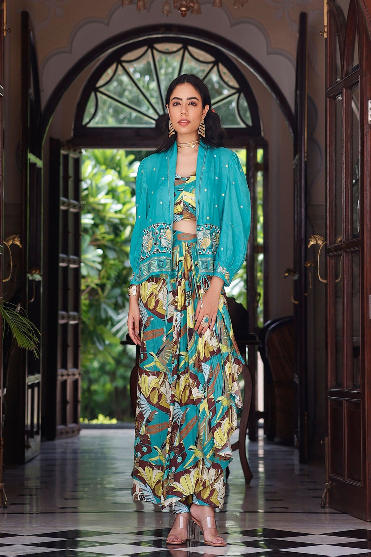 Woman in a colorful outfit standing in a decorated hallway with plants outside.