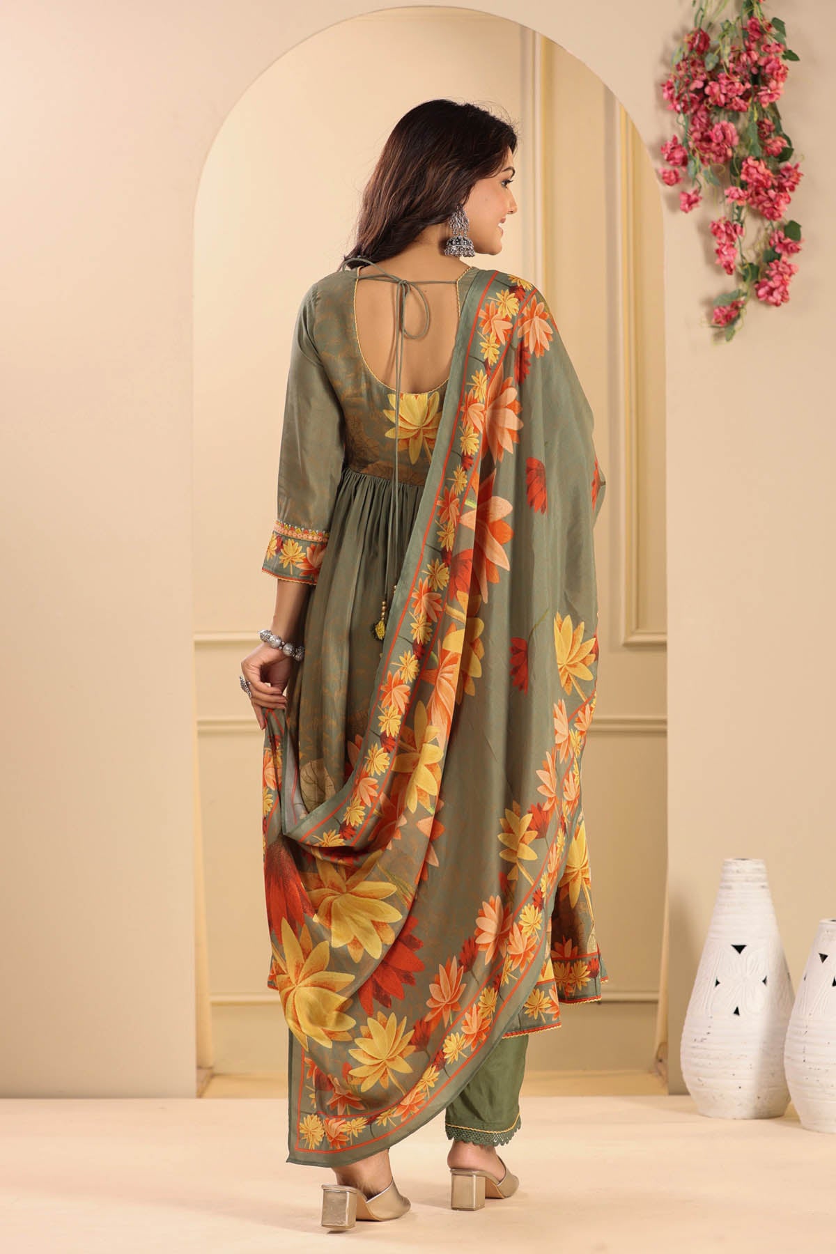Woman wearing a floral dress with a matching dupatta in a room with decorative elements.