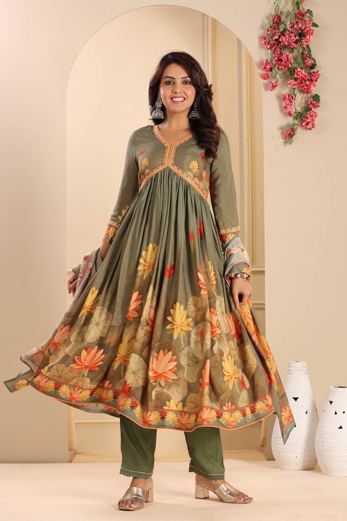 Woman wearing a green floral embroidered traditional outfit in a decorated room.