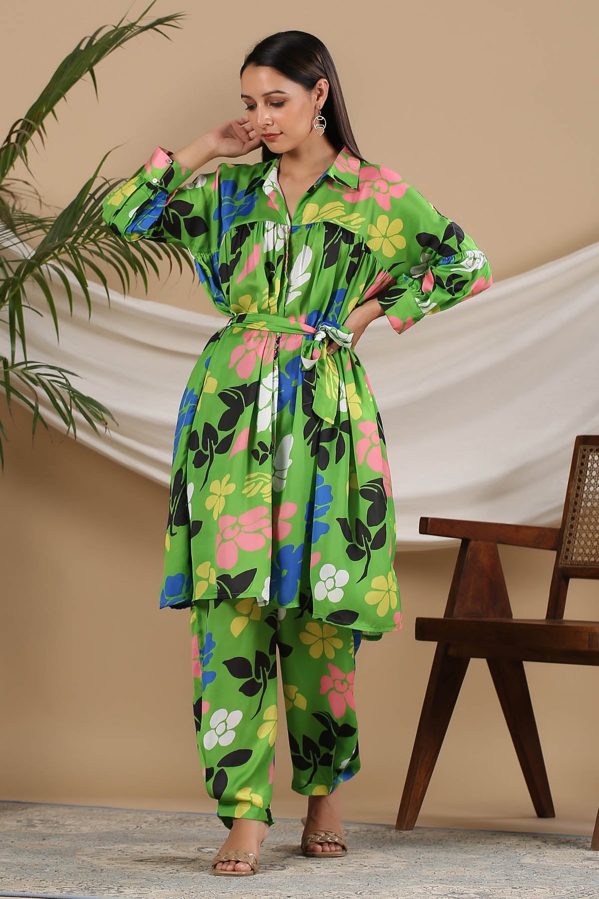 Woman wearing a colorful floral outfit standing in front of a beige curtain.