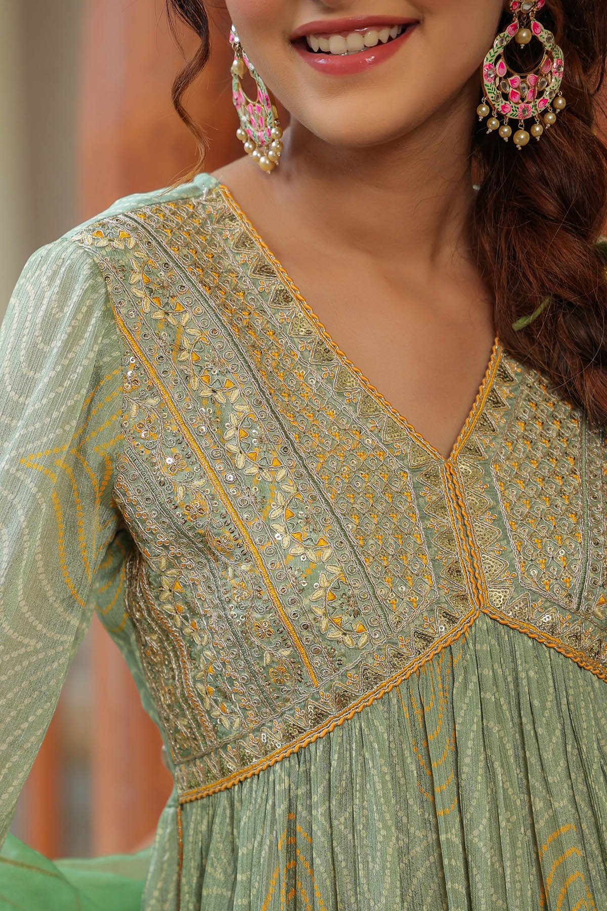 Woman wearing a green embroidered dress with gold details, smiling.