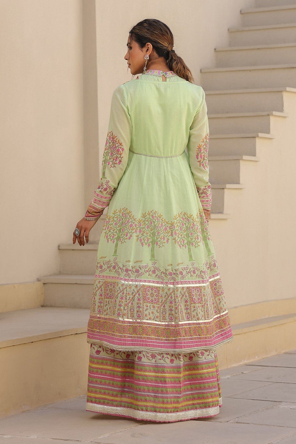 Woman in a light green traditional outfit standing on a staircase.
