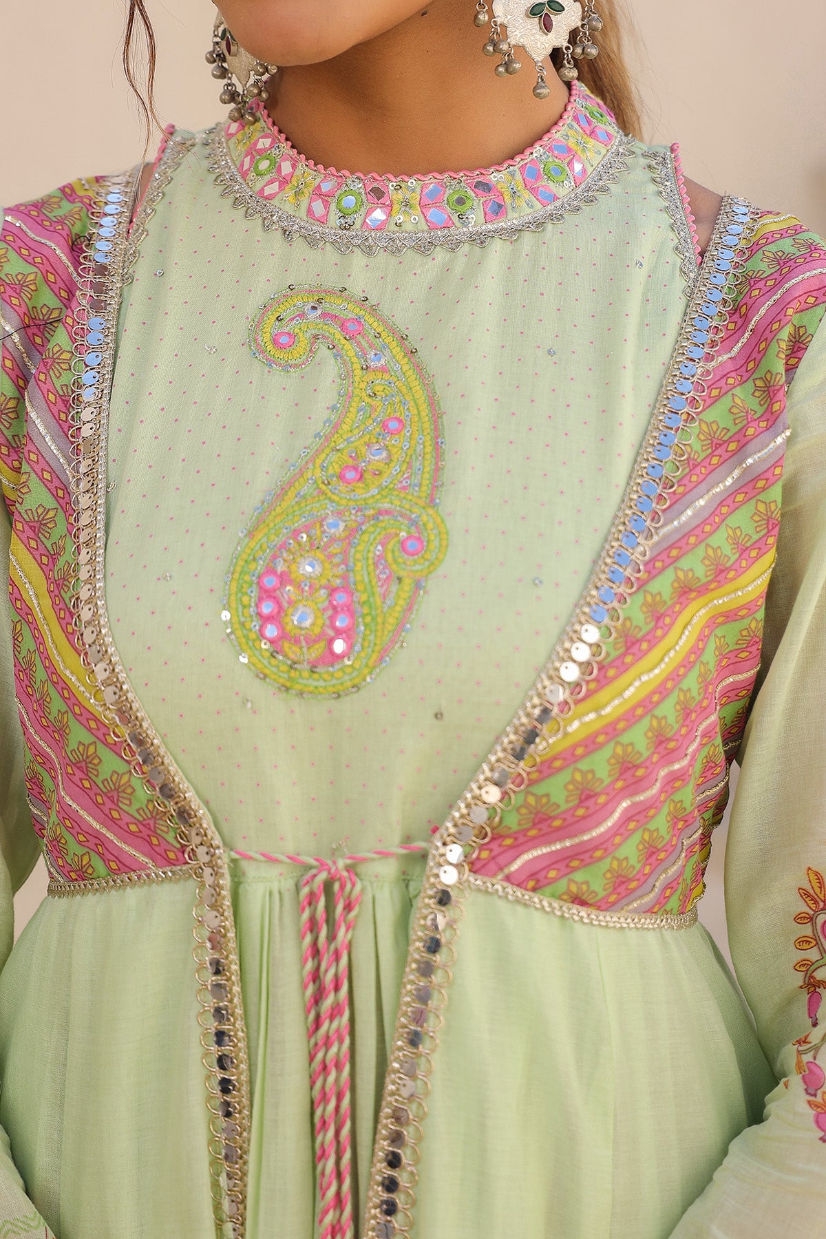 Light green traditional outfit with intricate pink and yellow embroidery on a beige background