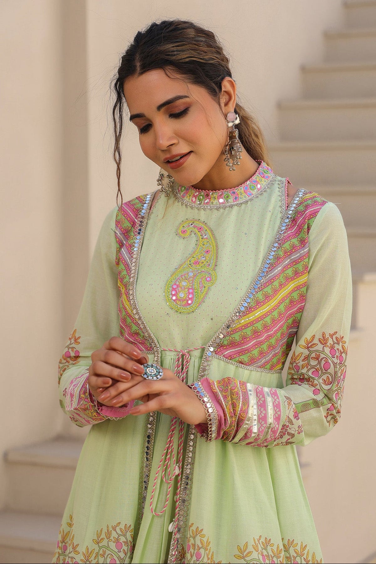 Woman in a light green traditional outfit with colorful embroidery standing on steps.