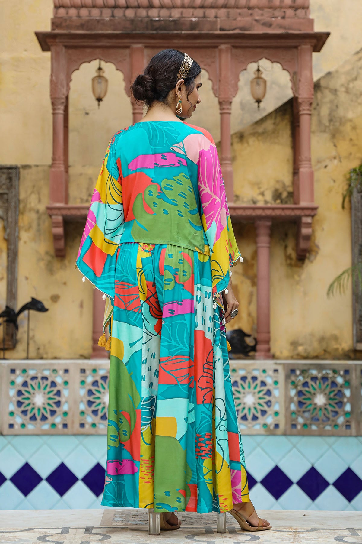 Woman in a colorful traditional outfit standing in front of a decorative wall.