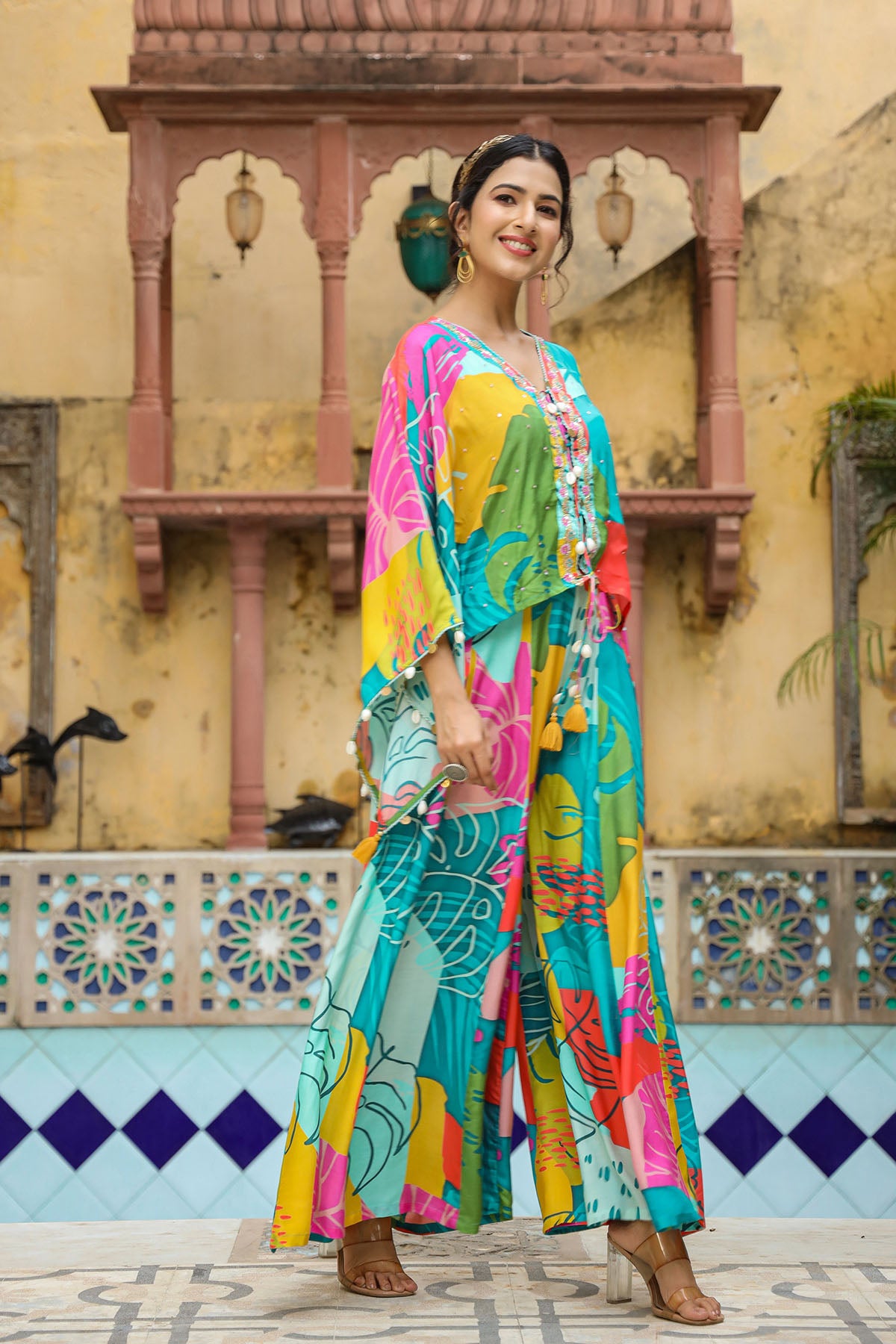 Woman in a colorful outfit standing in front of a decorative wall.