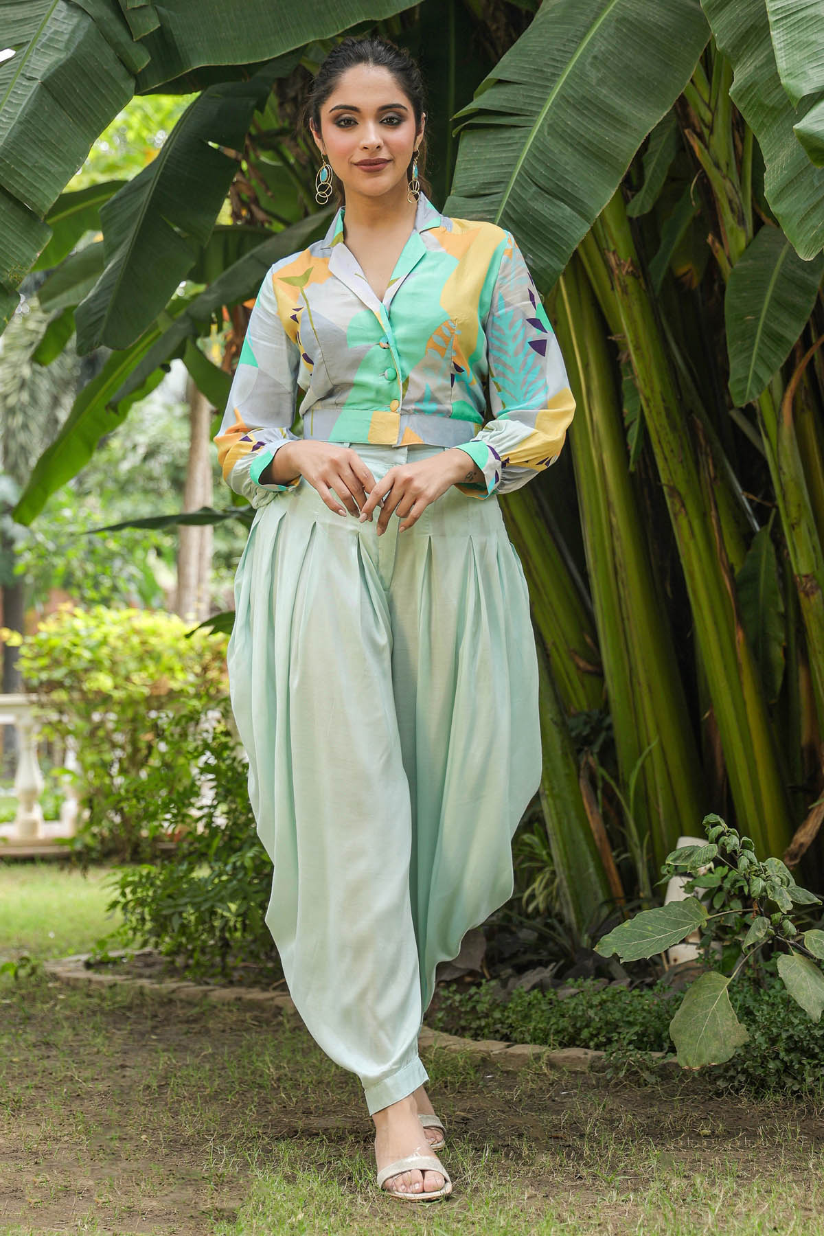 Woman in a light green outfit standing in a garden with large leaves.