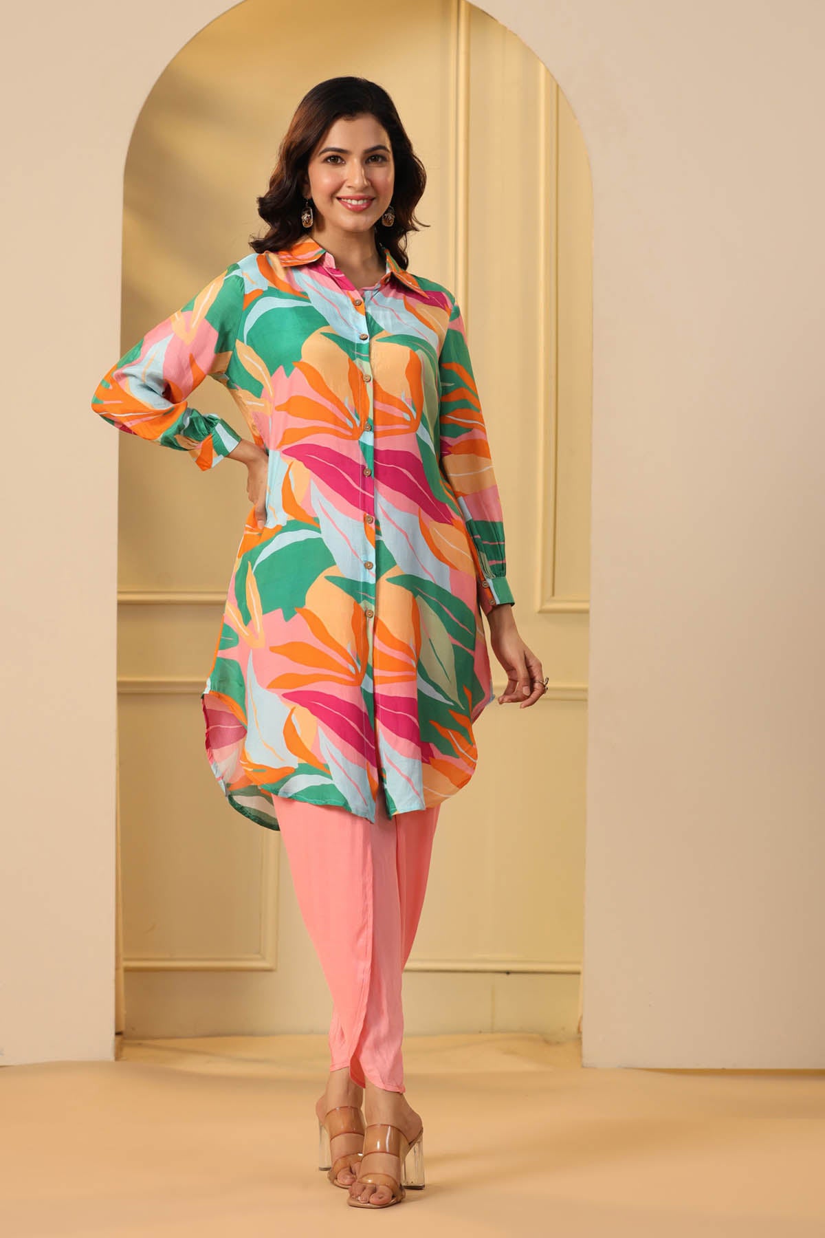 Woman wearing a colorful patterned shirt and pink pants standing in a doorway.