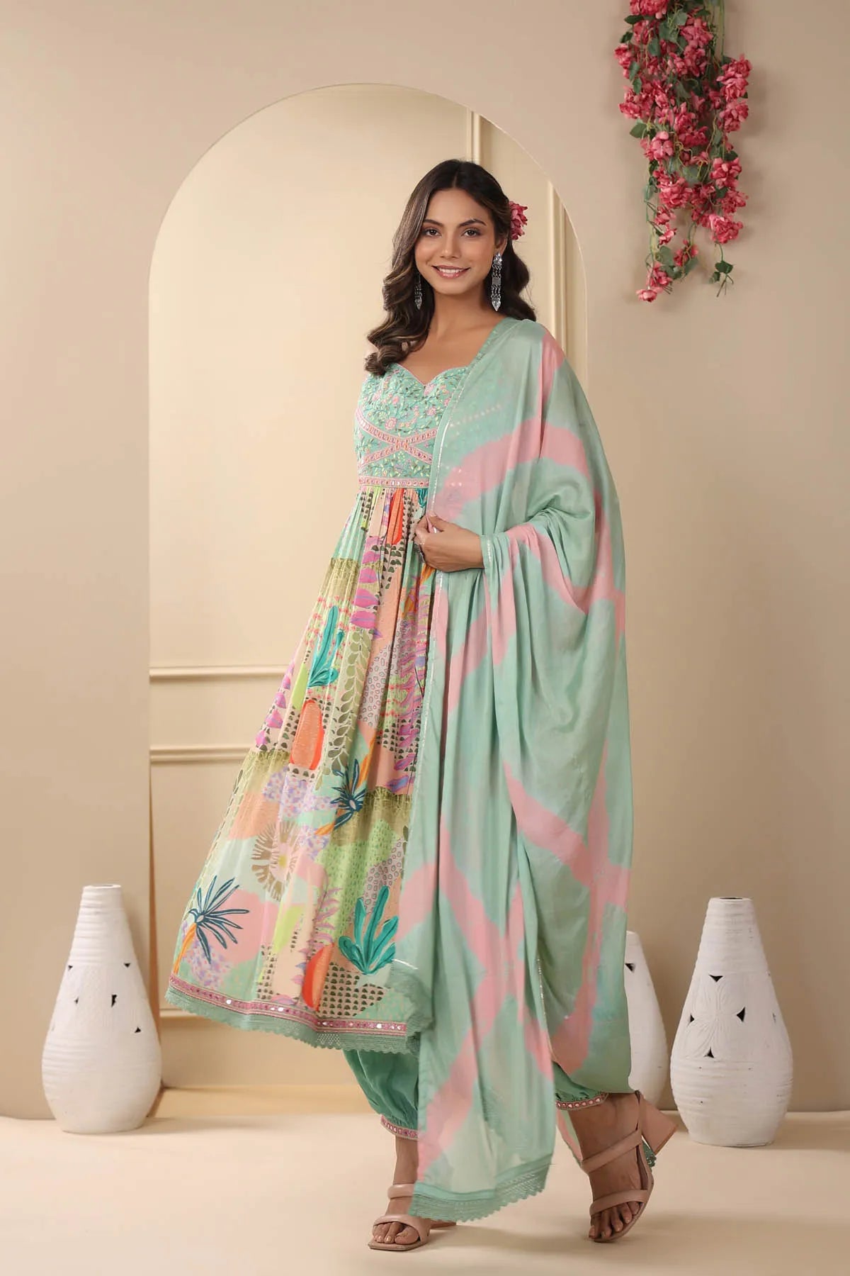 Woman in a light green dress with colorful patterns standing in a decorated room.