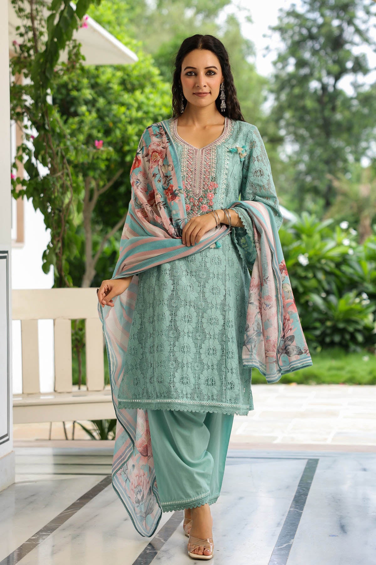 Woman in a light green traditional outfit with a floral dupatta standing outdoors.