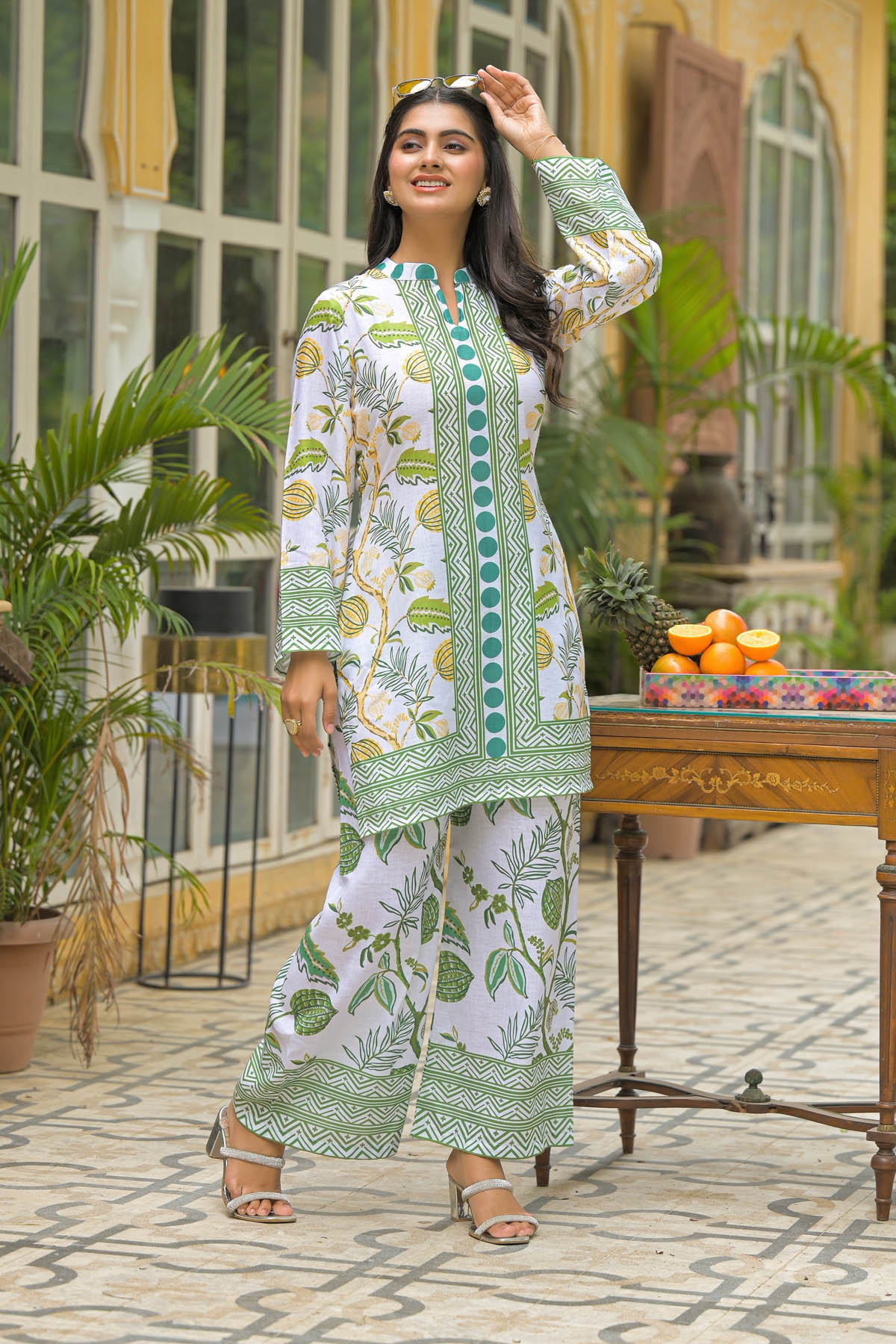 Woman in a floral outfit standing outdoors with plants and a table in the background