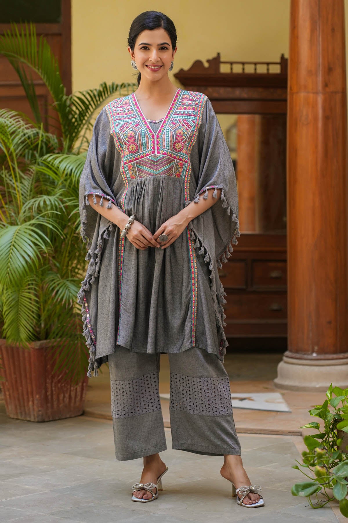 Woman wearing a traditional outfit with intricate patterns in an indoor setting.