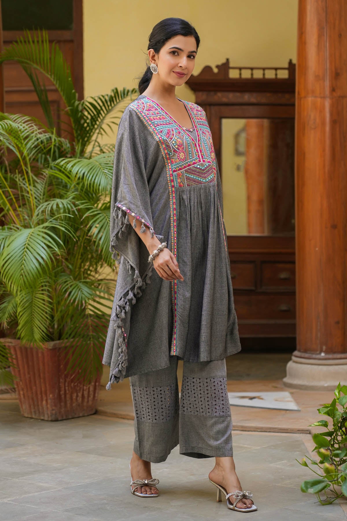 Woman in a traditional outfit standing in an indoor setting with plants.