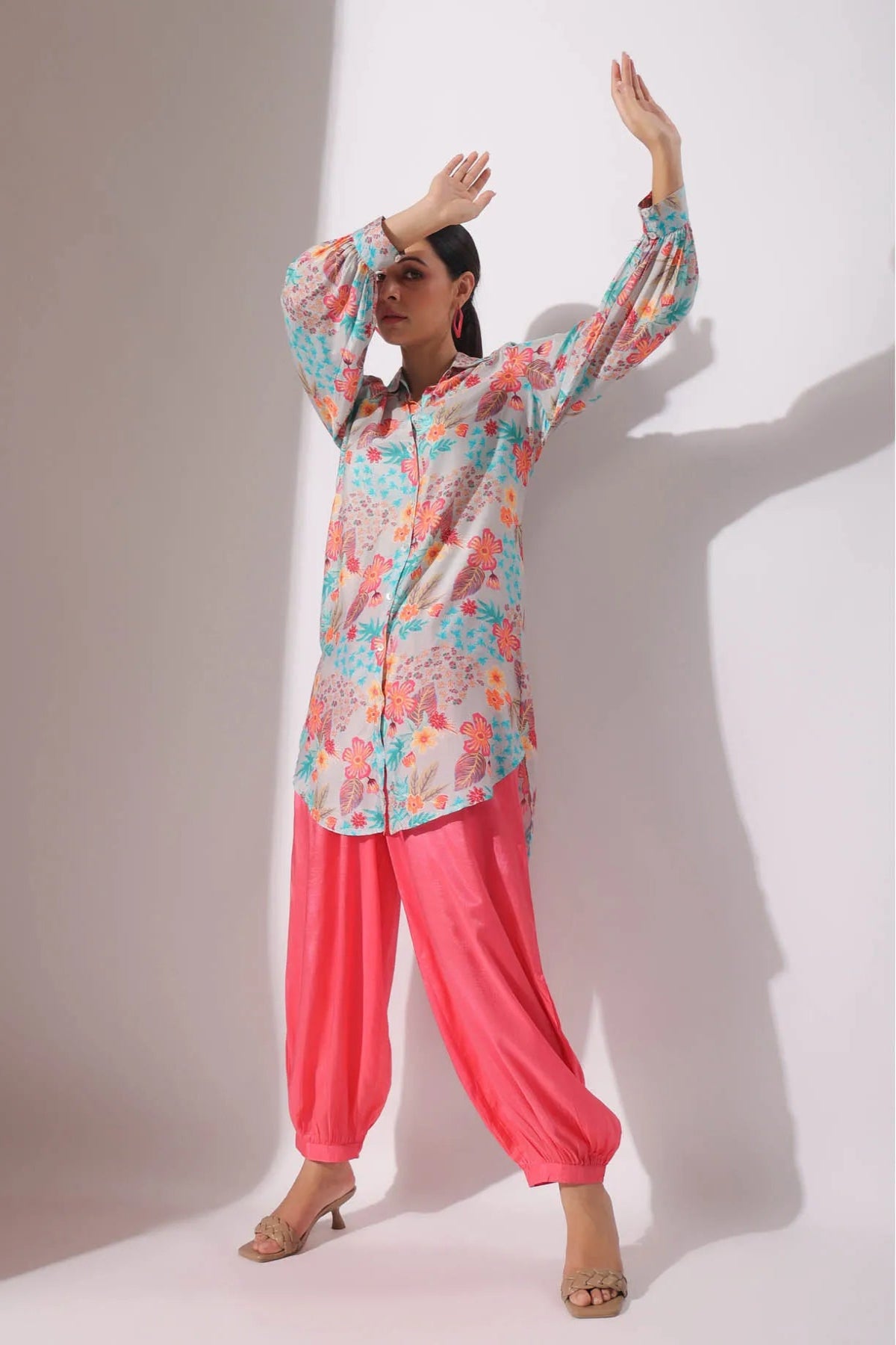 Woman wearing a colorful floral top and pink pants against a white background