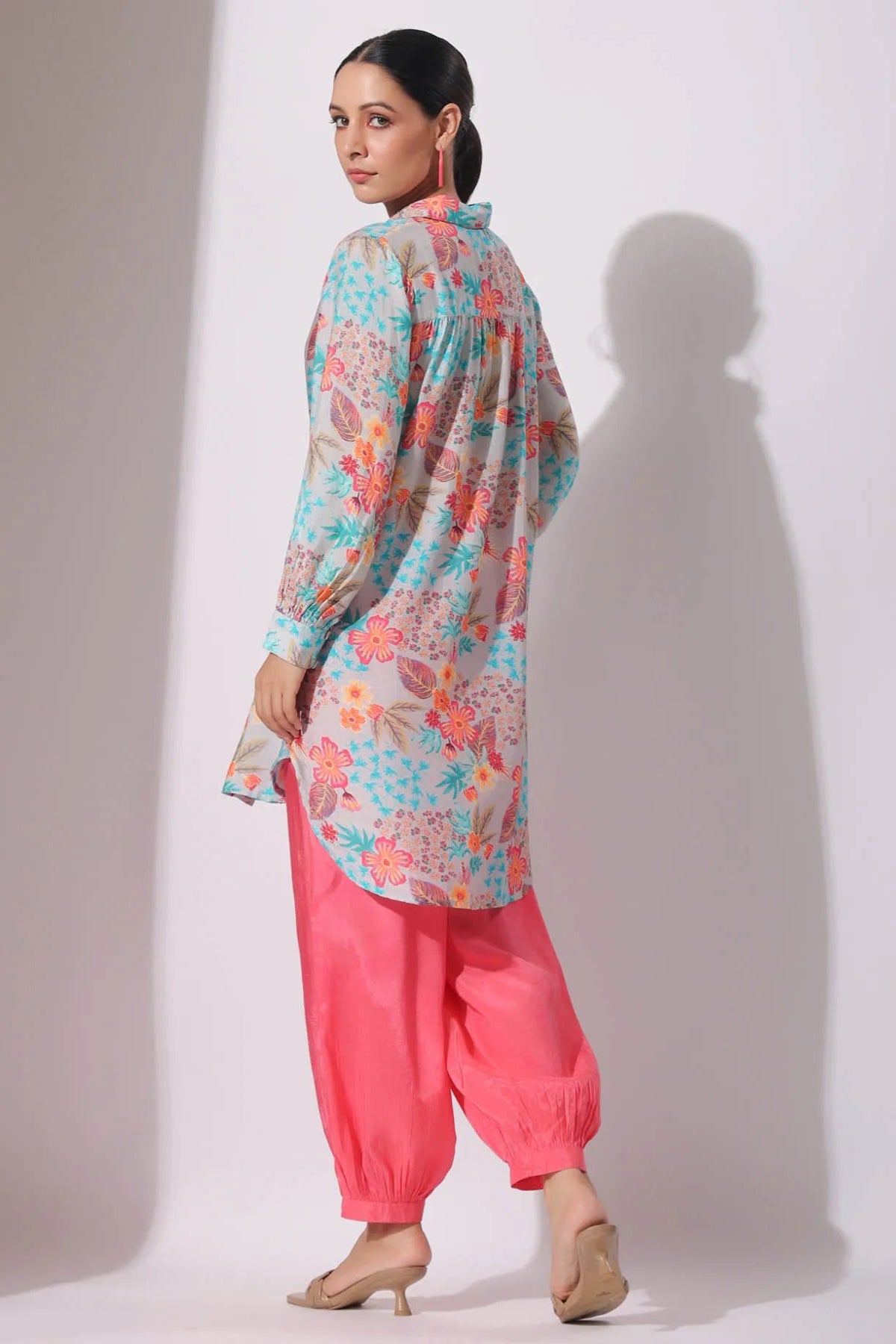 Woman wearing a floral top and pink pants against a white background