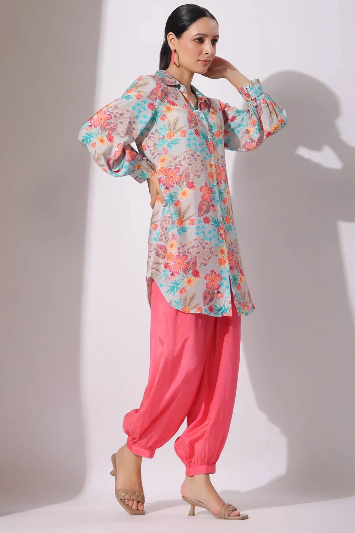 Woman wearing a floral top and pink pants against a white background