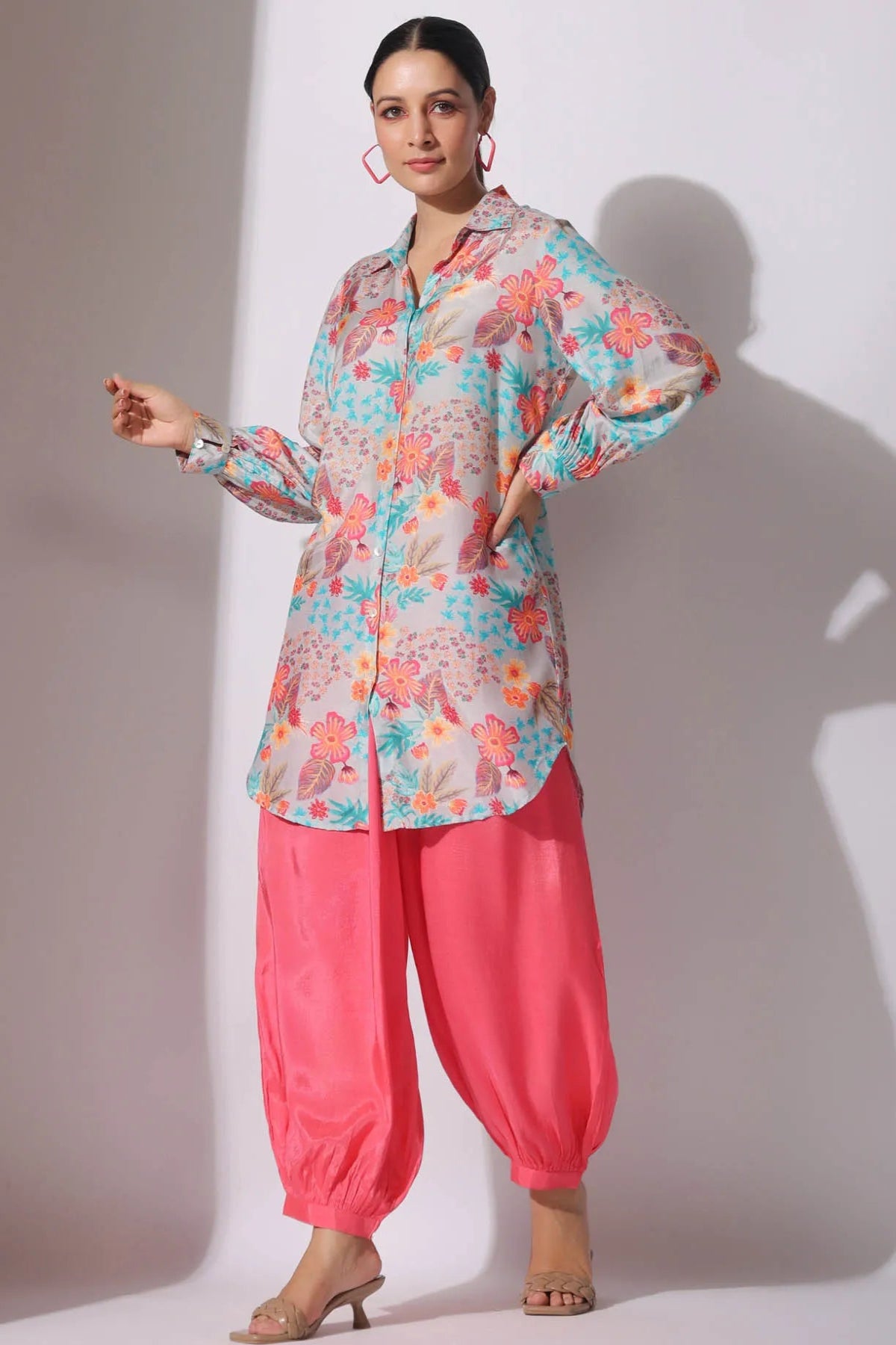 Woman wearing a floral blouse and pink pants against a white background