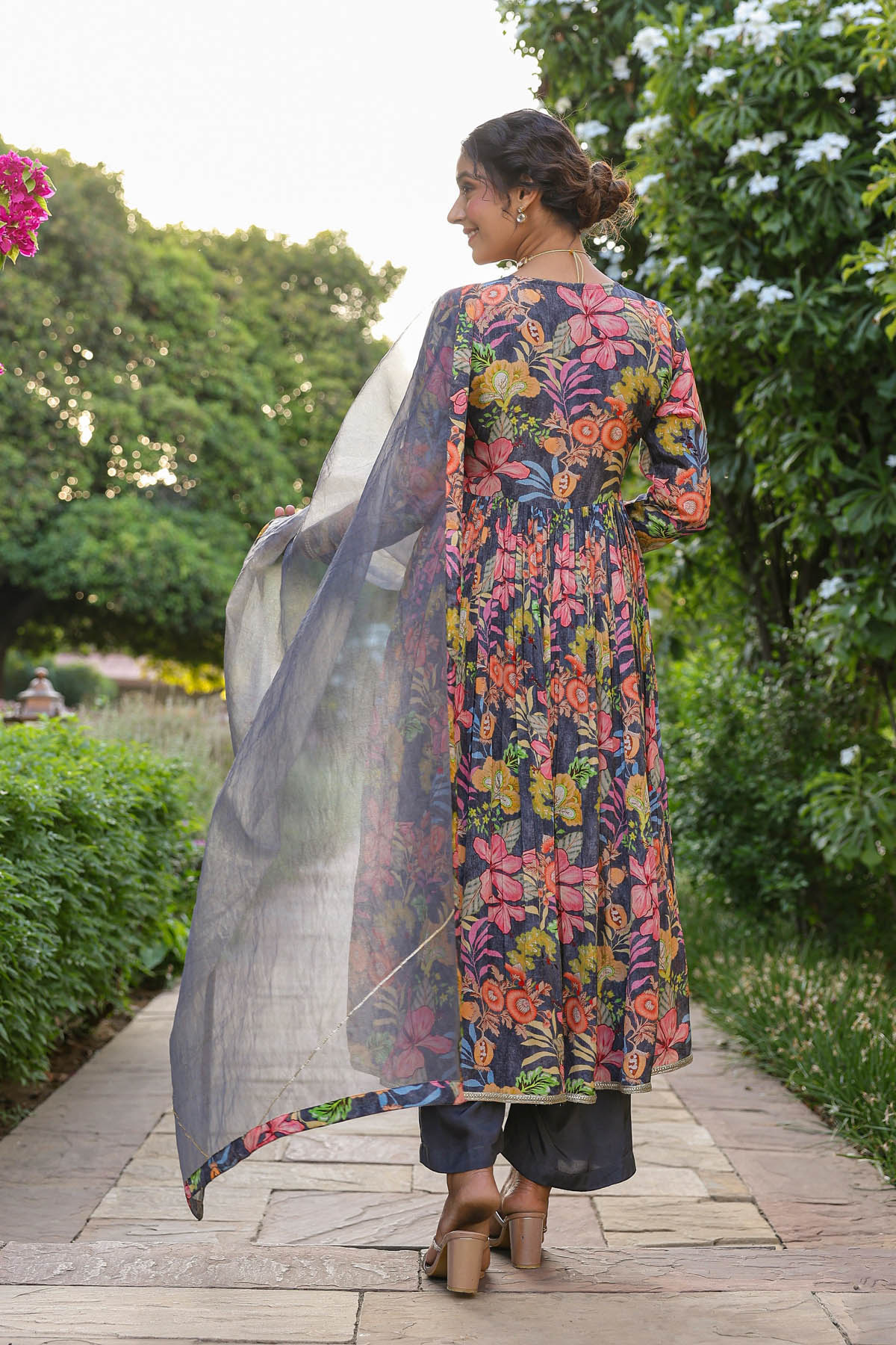 Woman wearing a colorful floral dress with a sheer overlay in an outdoor setting.