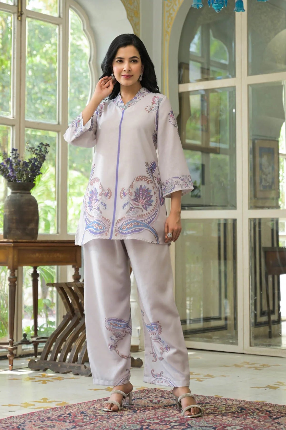 Woman wearing a light-colored outfit with floral patterns in a room with large windows.