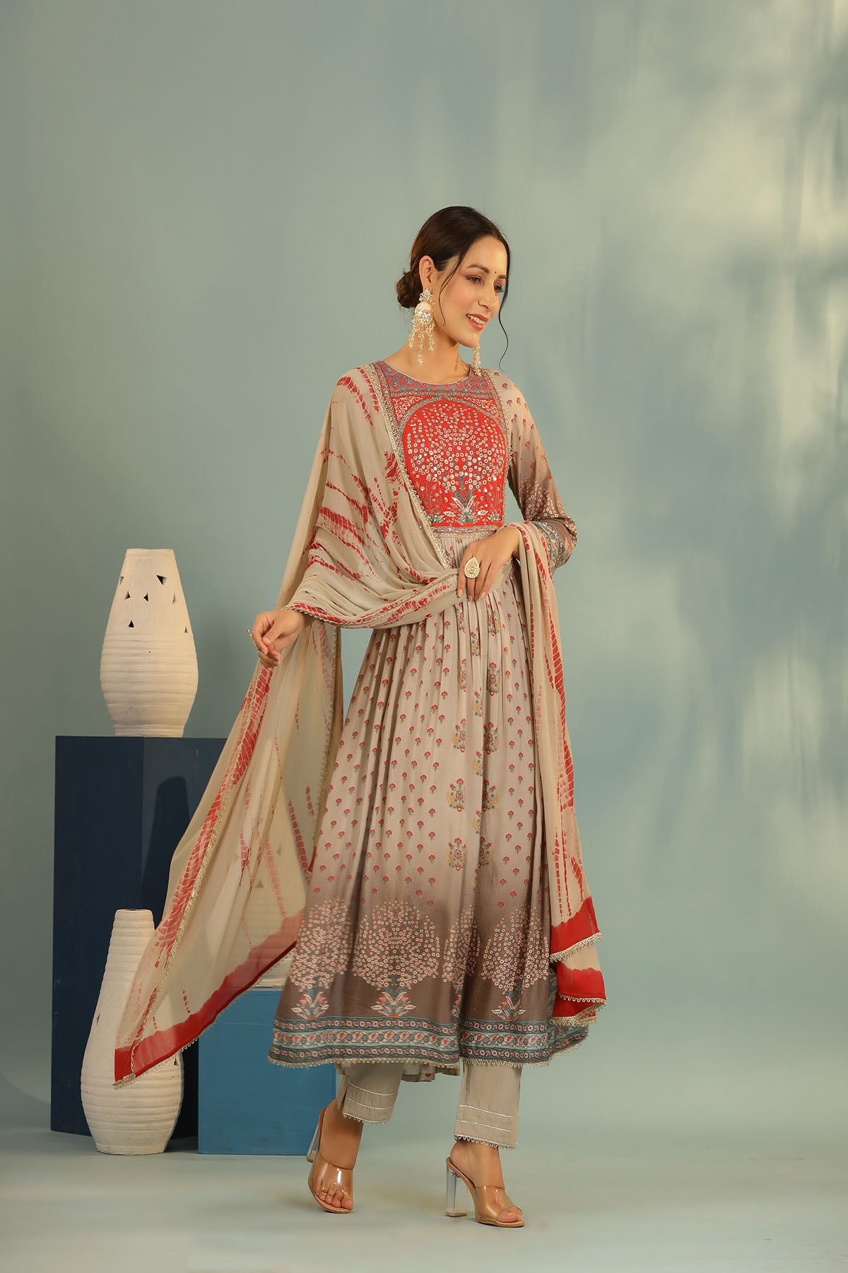 Woman wearing a traditional outfit with a red and beige pattern against a gray background