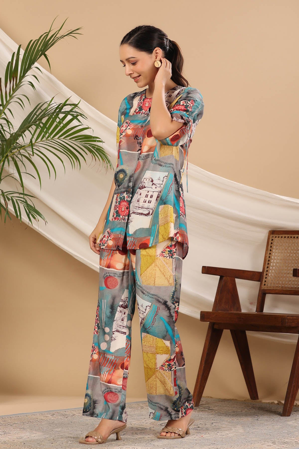 Woman wearing a colorful outfit in a room with a plant and wooden chair.