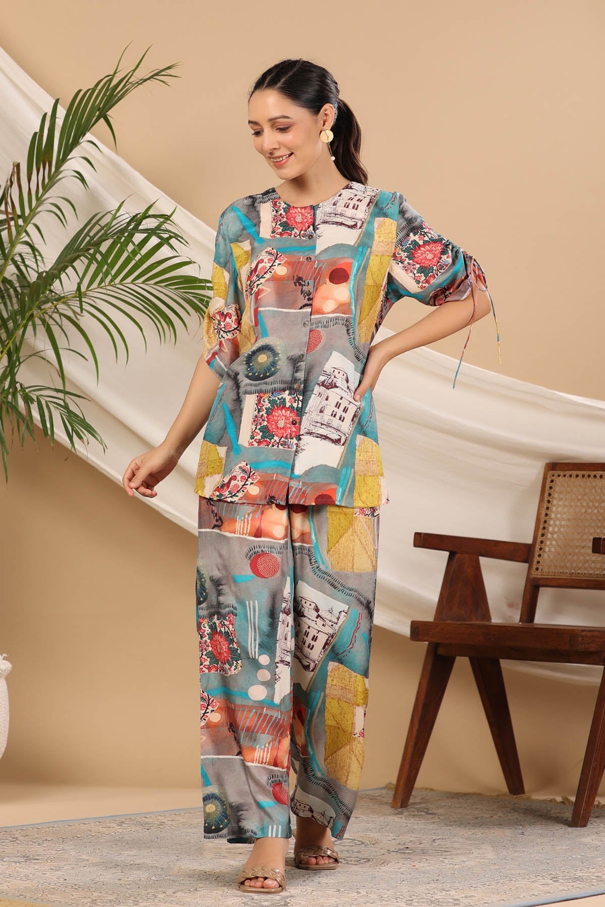Woman wearing a colorful outfit with a patterned design in a room with a plant and wooden chair.