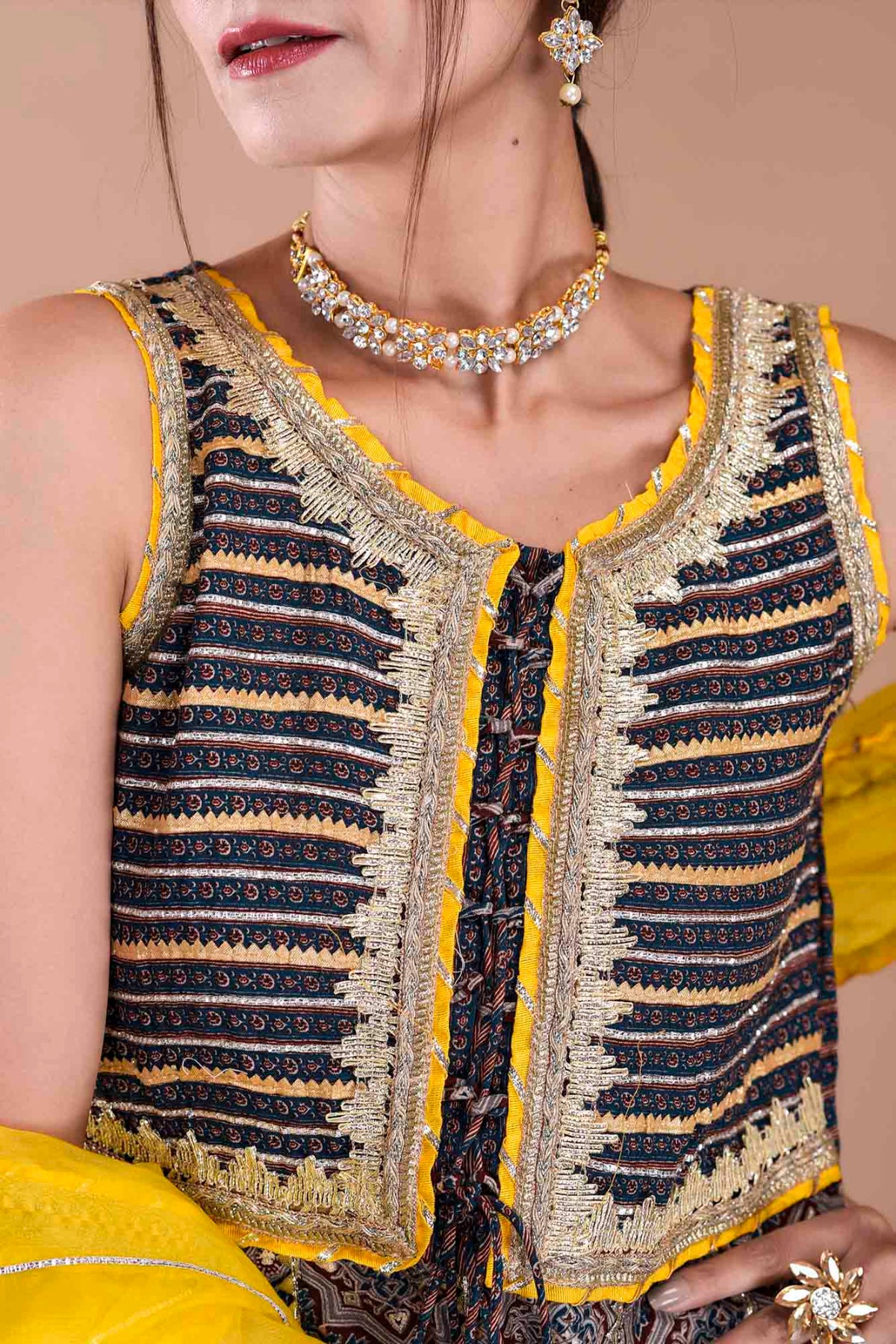 Woman wearing a patterned top with yellow trim and jewelry on a beige background