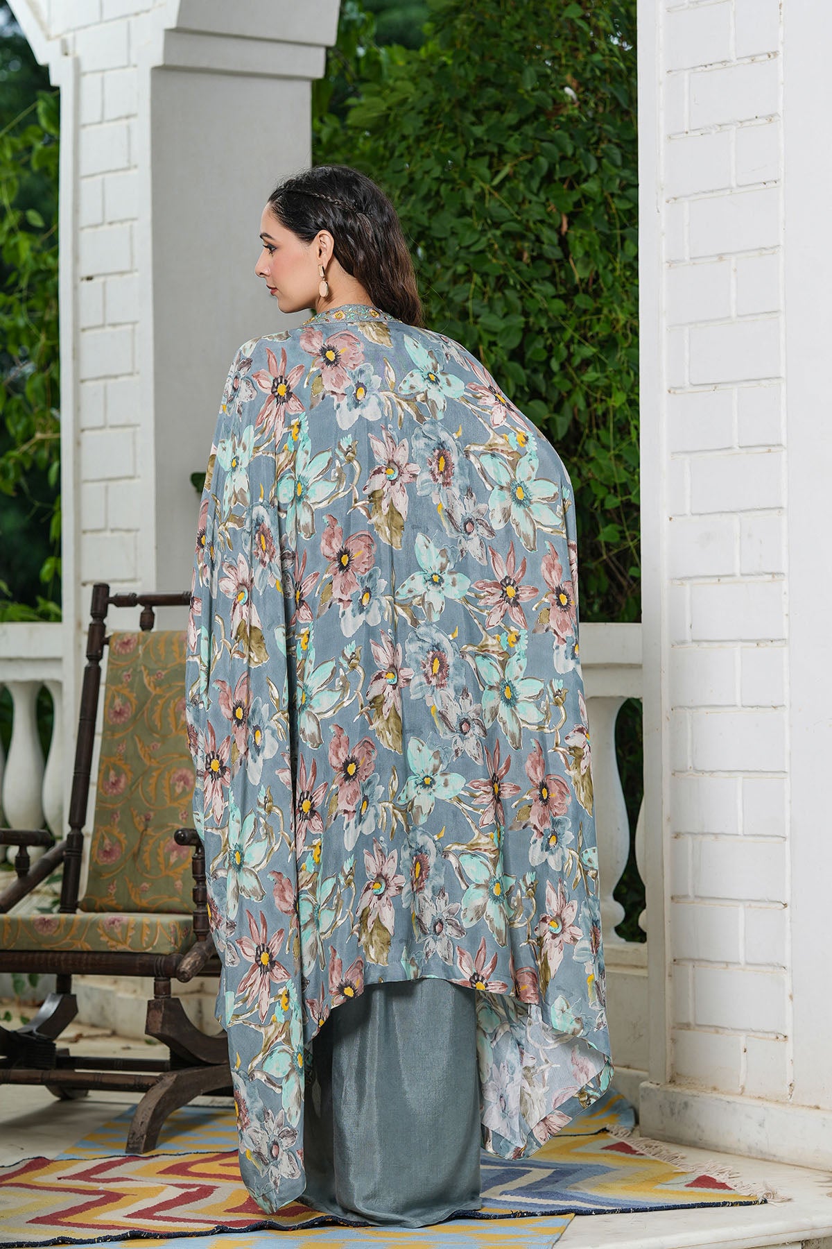 Woman wearing a floral kimono-style garment standing on a porch.