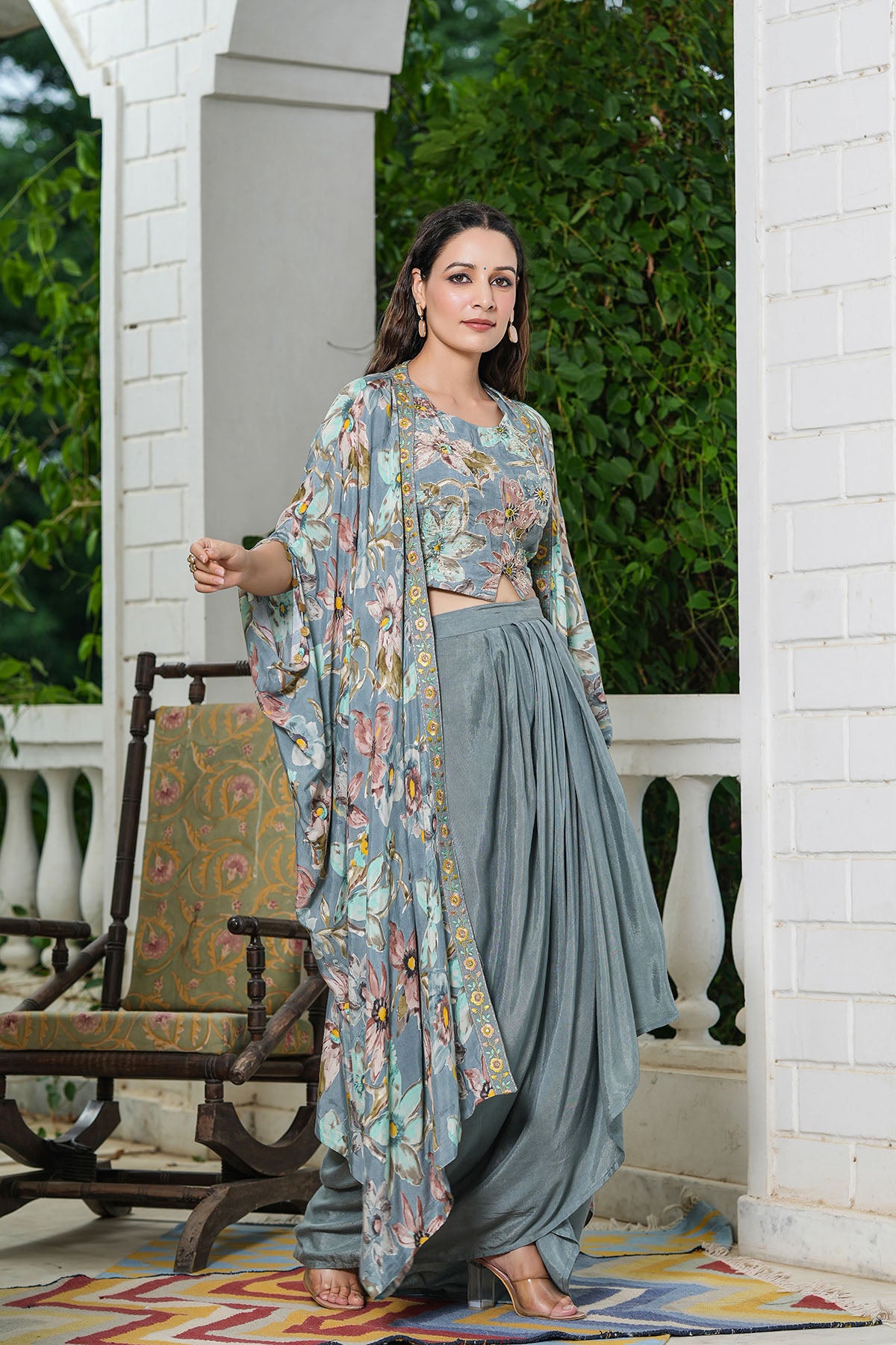 Woman in a floral kimono and gray dhoti standing on a porch with greenery in the background