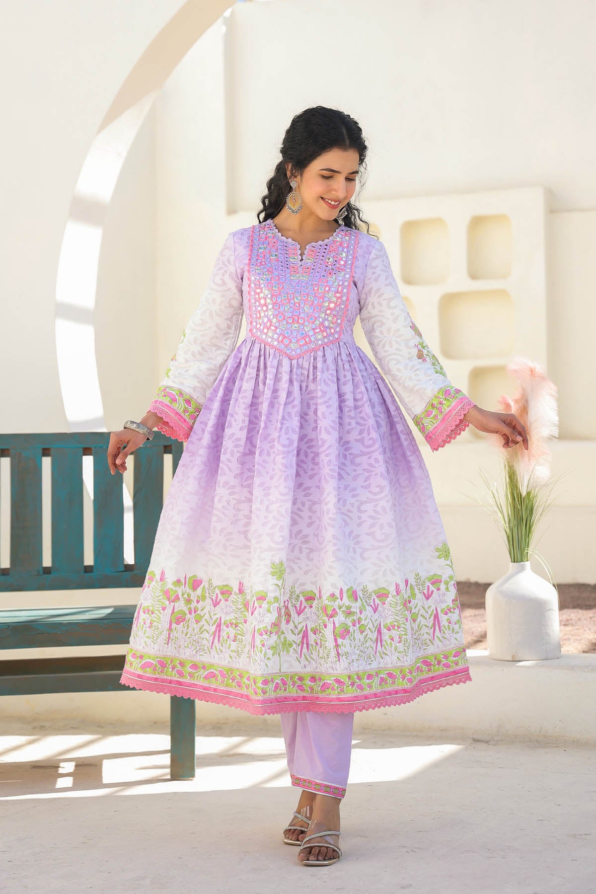 Woman wearing a light purple and pink traditional outfit with floral patterns in an outdoor setting.