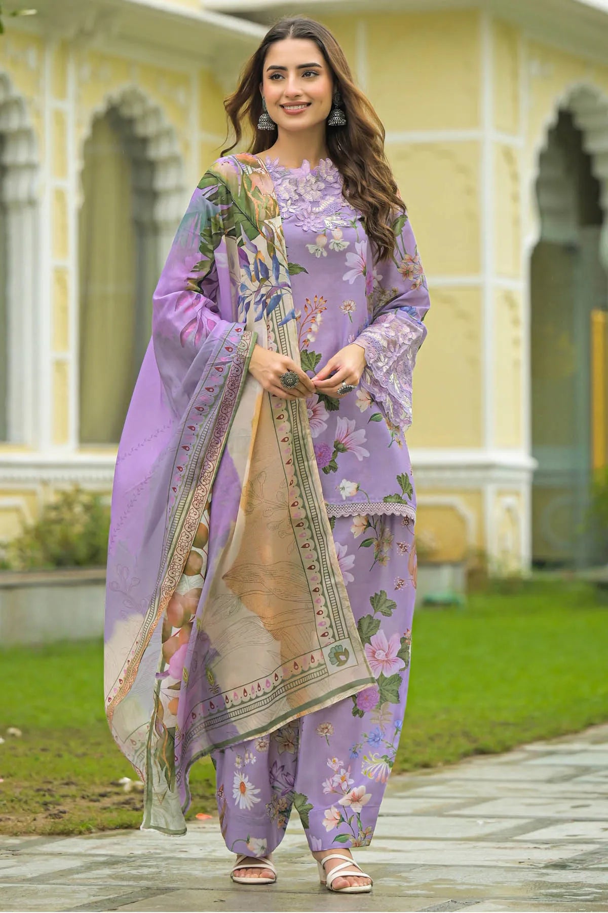 Woman in a lavender traditional outfit with floral patterns standing in front of a building.