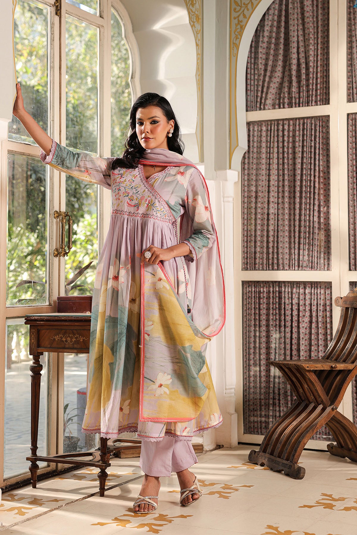 Woman in a traditional outfit standing in a decorated room with large windows.