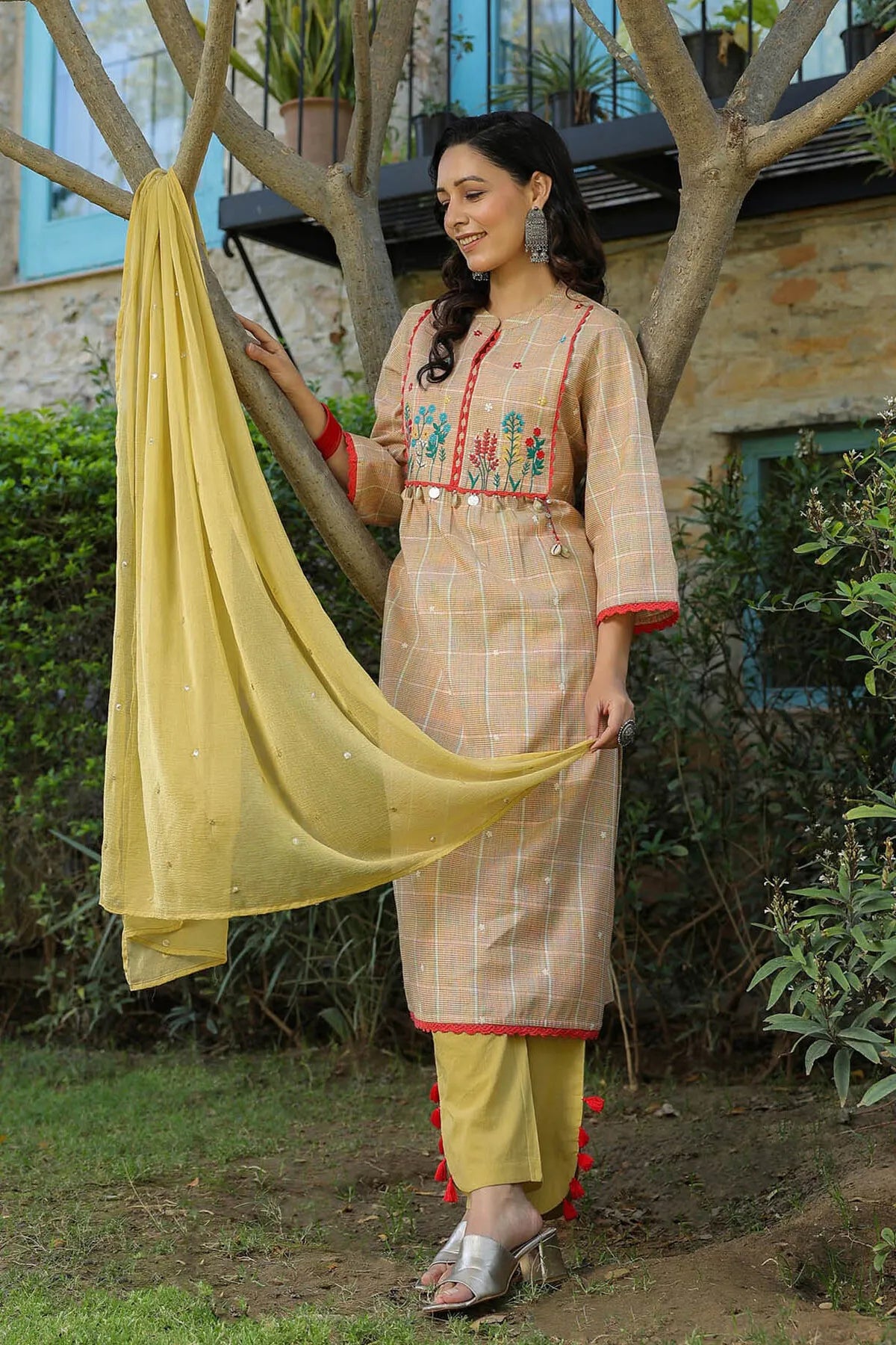 Woman in traditional outfit with yellow dupatta standing outdoors near a tree