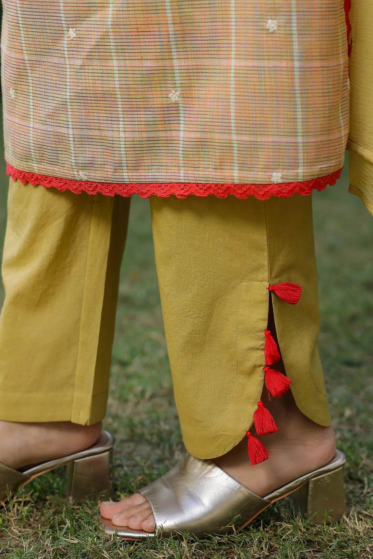 Traditional outfit with a checkered top and yellow pants with red tassels, worn outdoors.