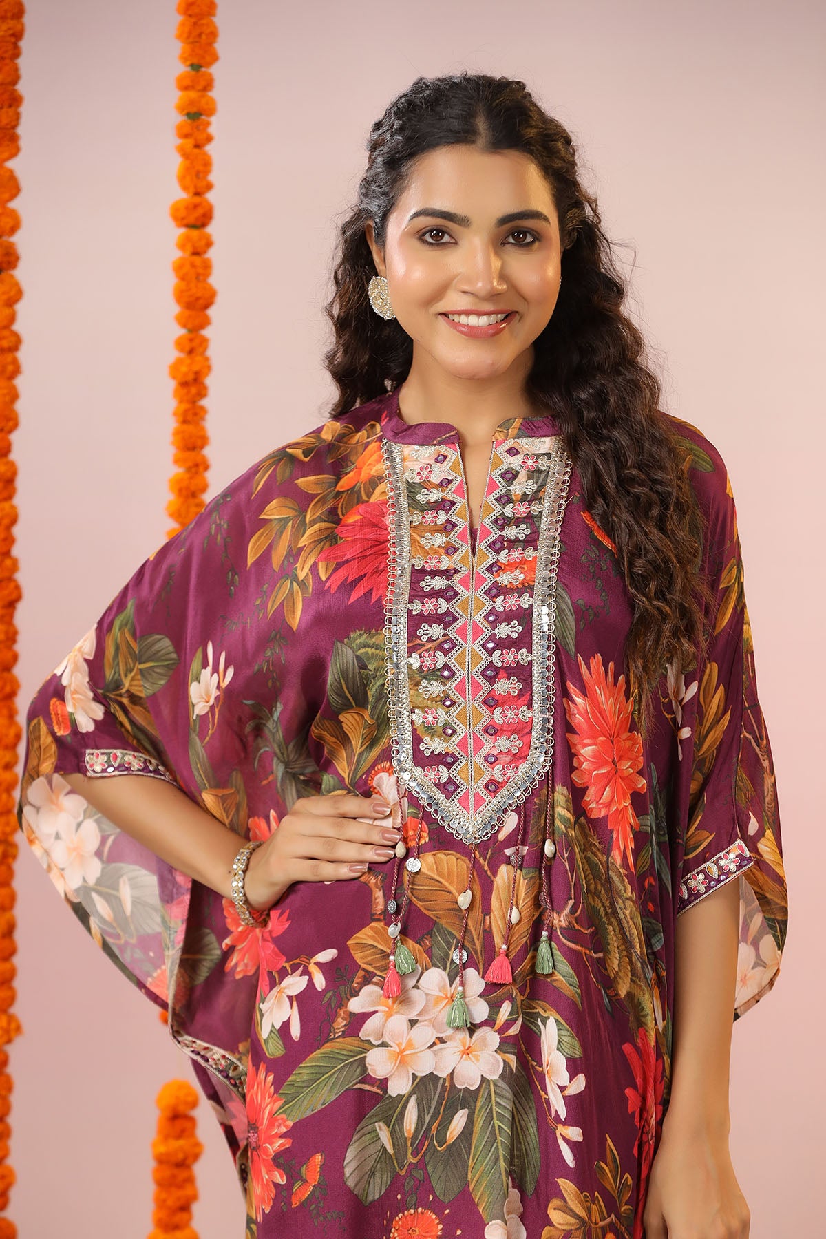 Woman wearing a colorful floral dress with intricate embroidery against a pink background