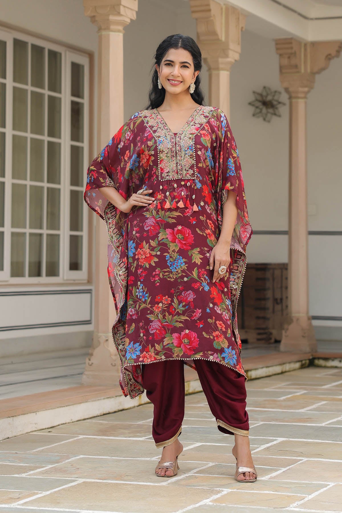 Woman wearing a floral dress and maroon pants standing in front of a building.
