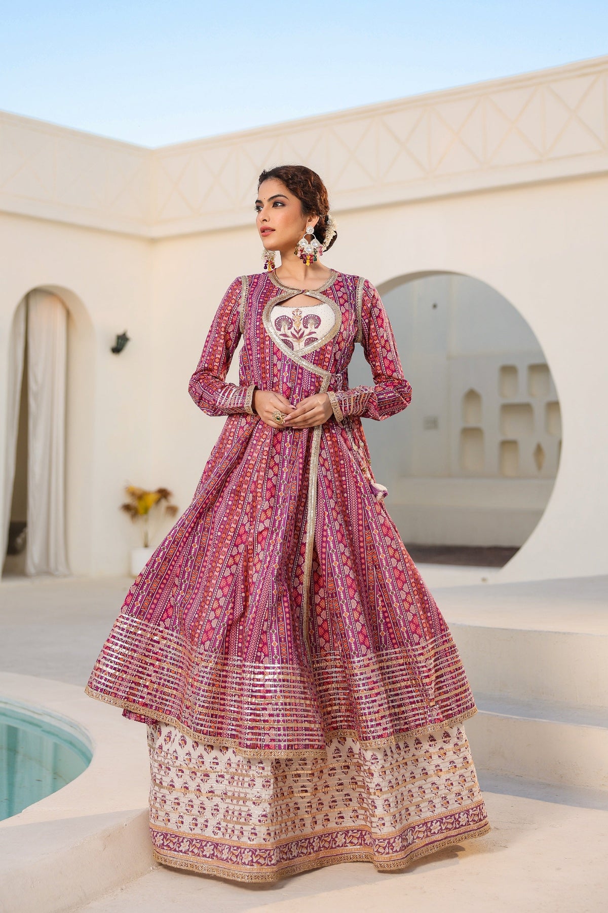 Woman in a traditional pink and white outfit standing in a decorative architectural setting.