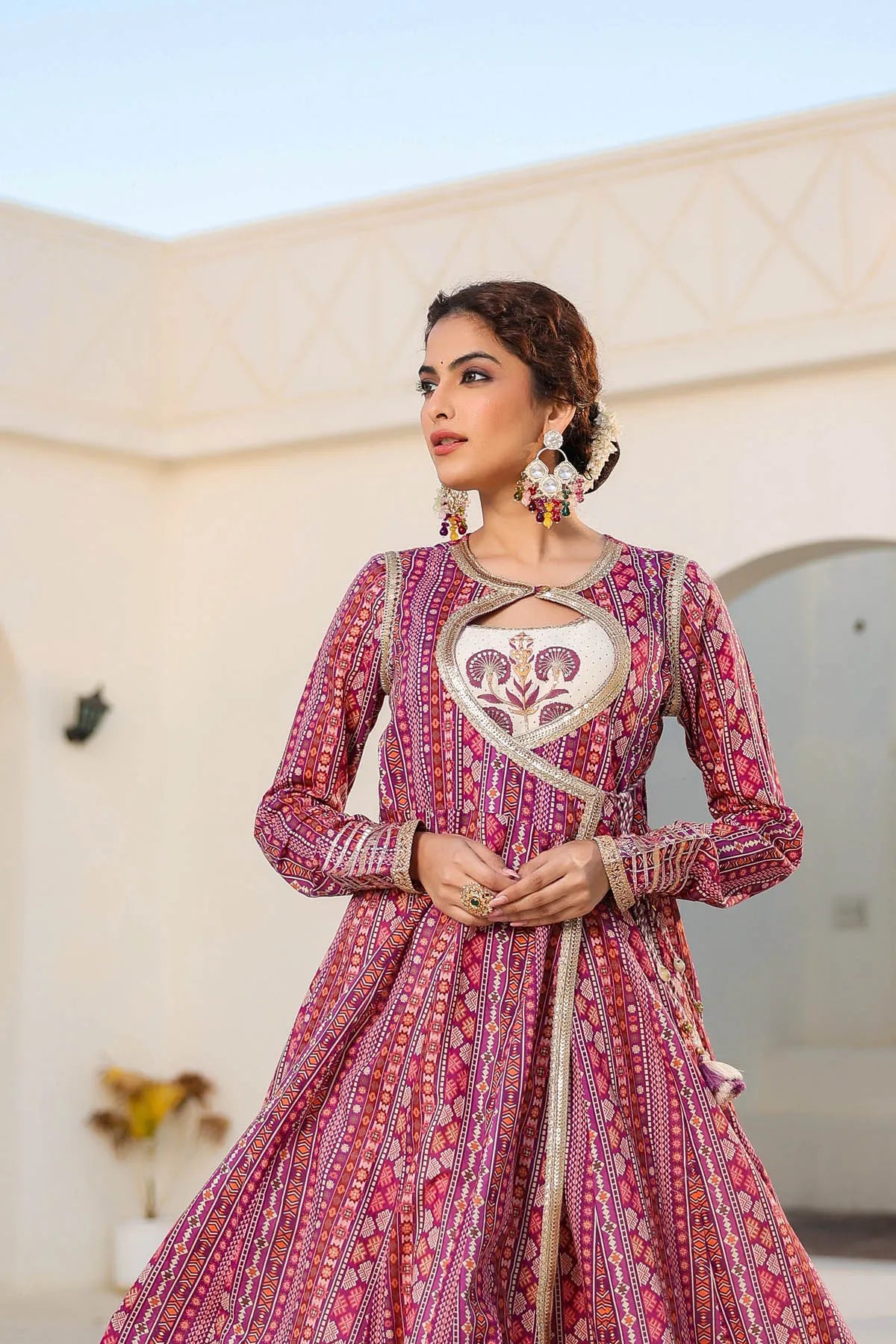 Woman wearing a traditional pink and red patterned dress with a decorative belt against a beige wall.