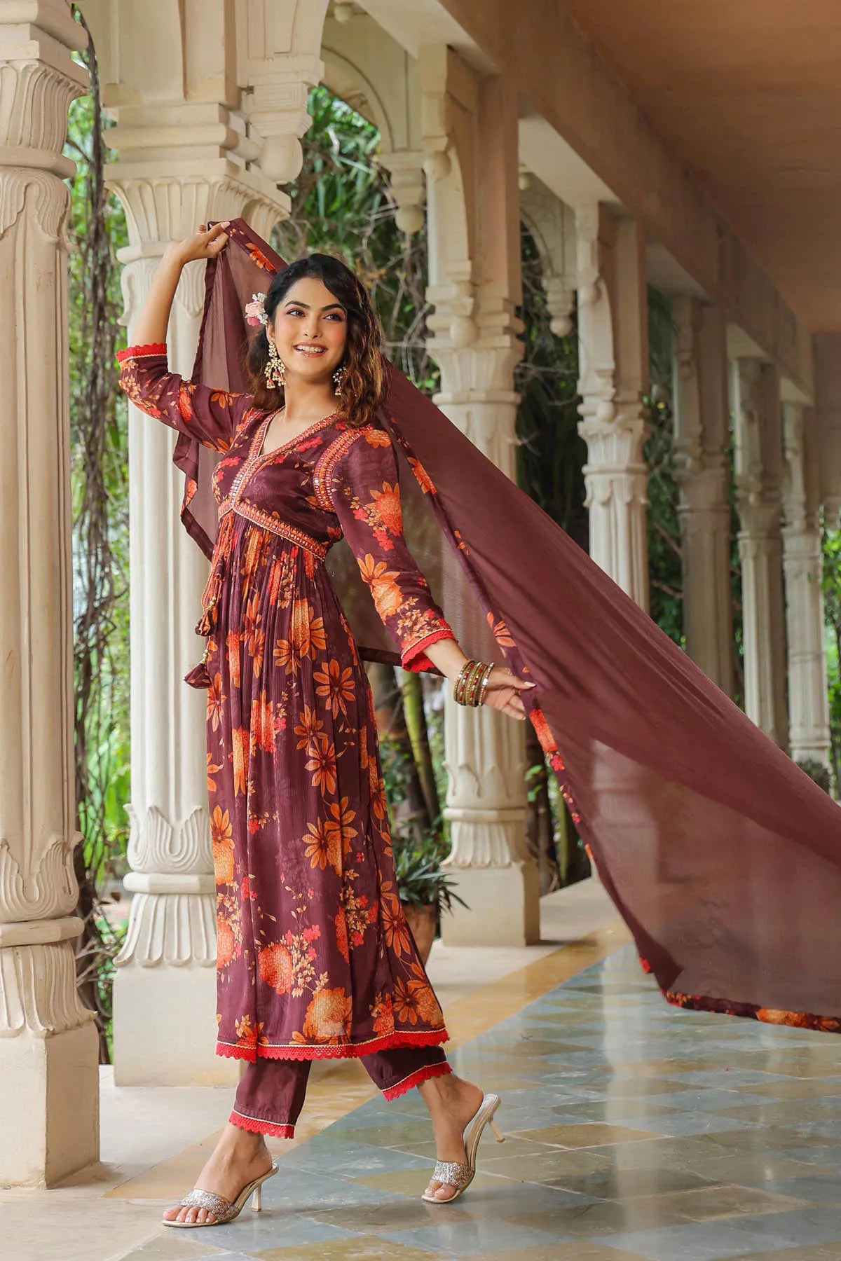 Woman in a traditional outfit with a long scarf standing in an elegant outdoor setting.