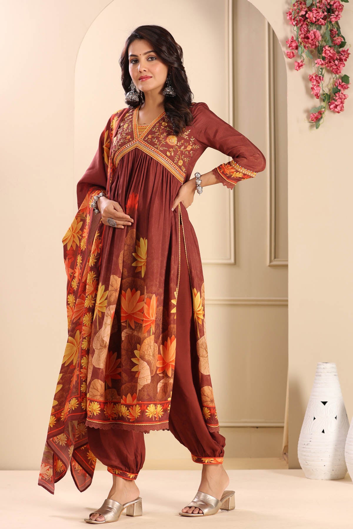 Woman wearing a maroon traditional outfit with floral patterns in a decorated room.