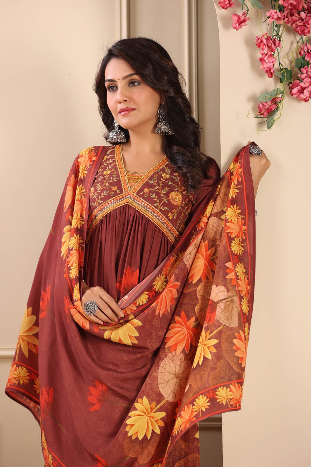 Woman wearing a traditional maroon saree with floral patterns against a neutral background