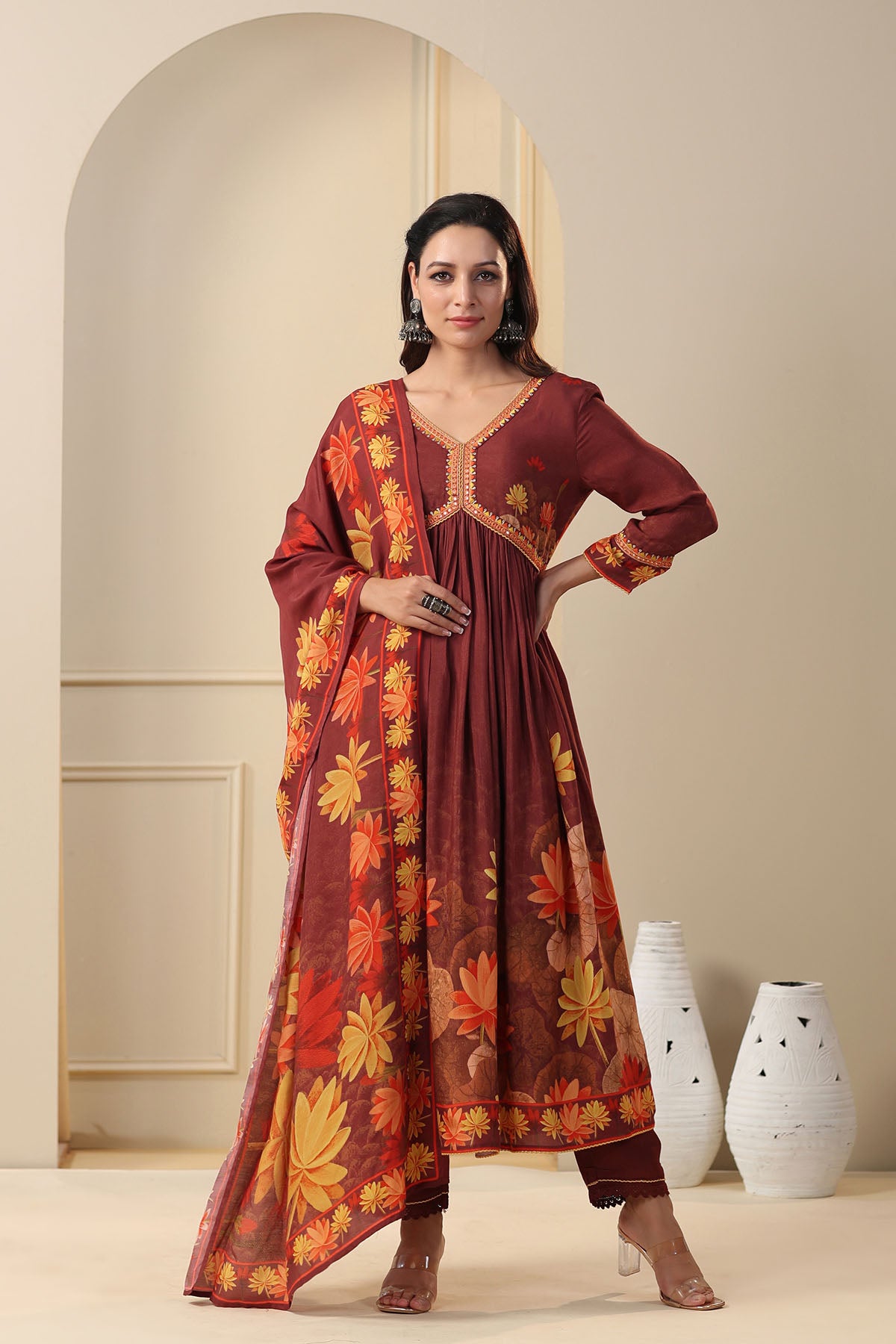 Woman wearing a maroon floral dress standing in a room with white vases.