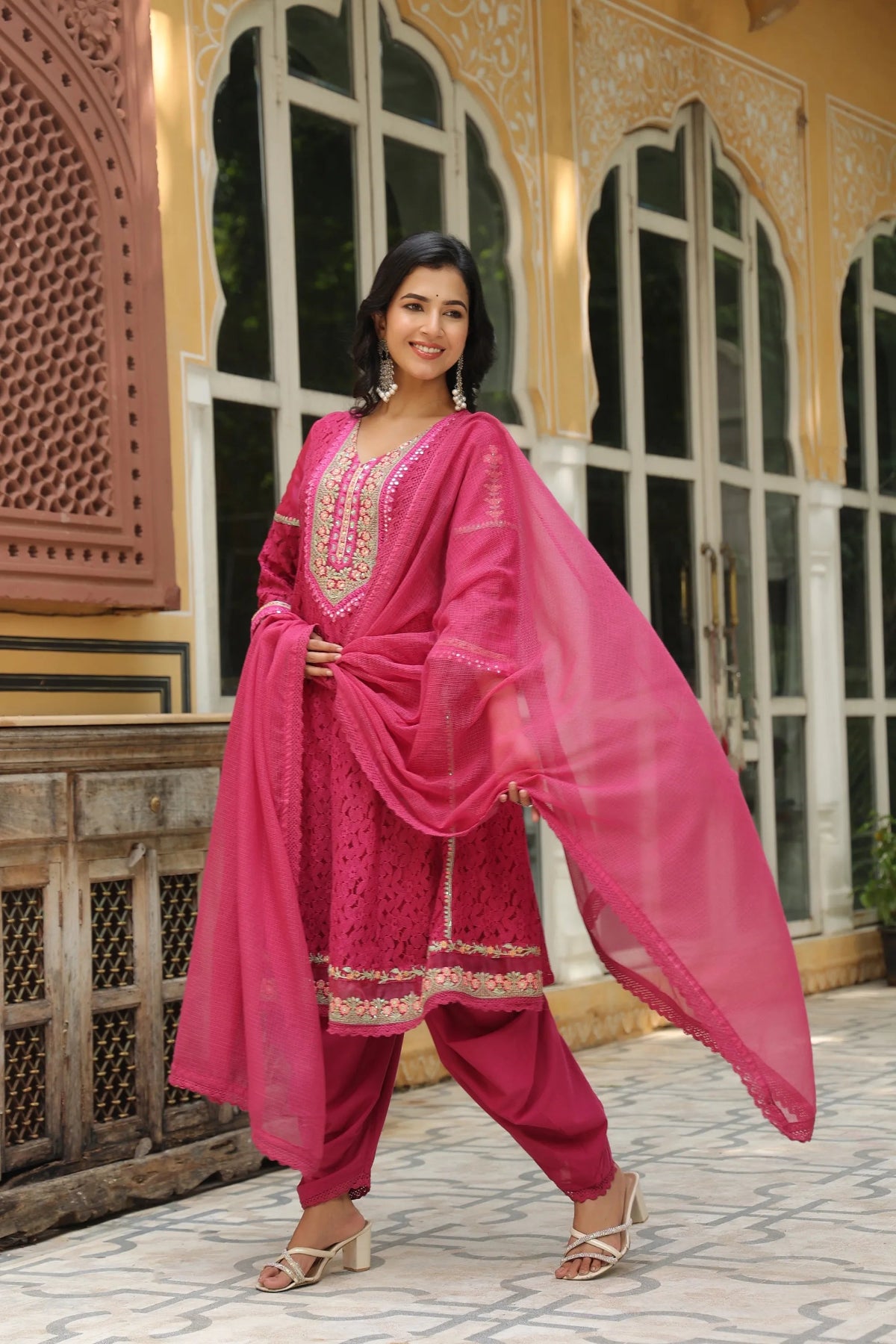 Woman in a bright pink traditional outfit standing in front of an ornate building.