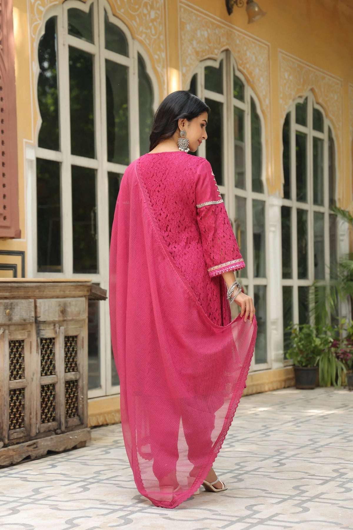 Woman in a pink traditional outfit standing in front of a decorative building with large windows.