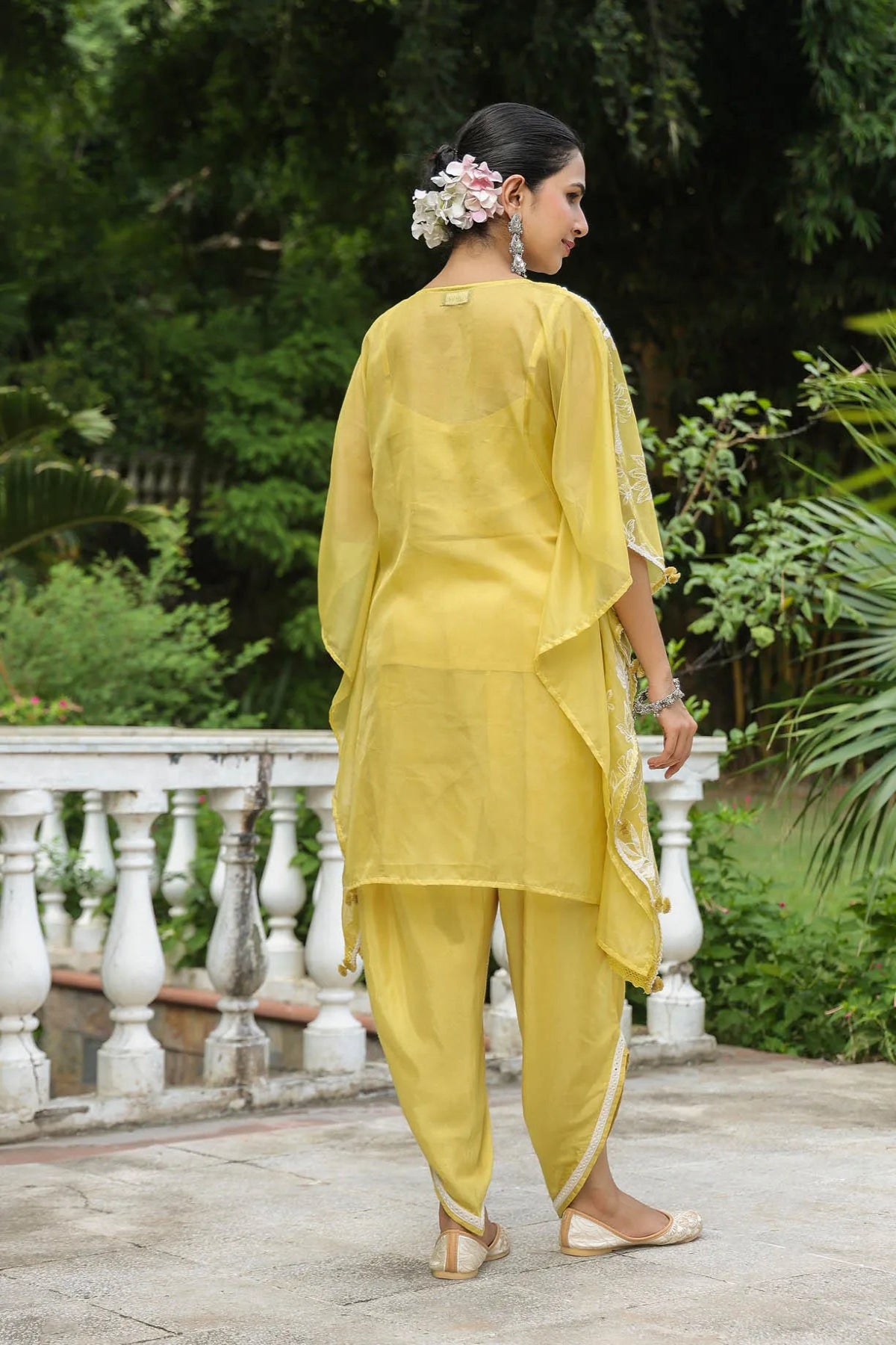 Woman in a yellow traditional outfit standing outdoors with greenery in the background