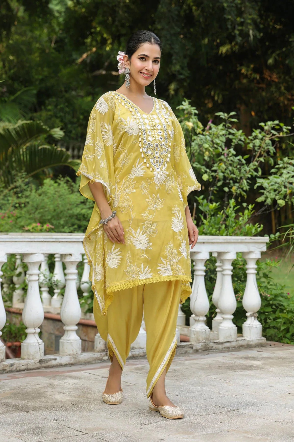 Woman in a yellow traditional outfit standing outdoors with greenery in the background