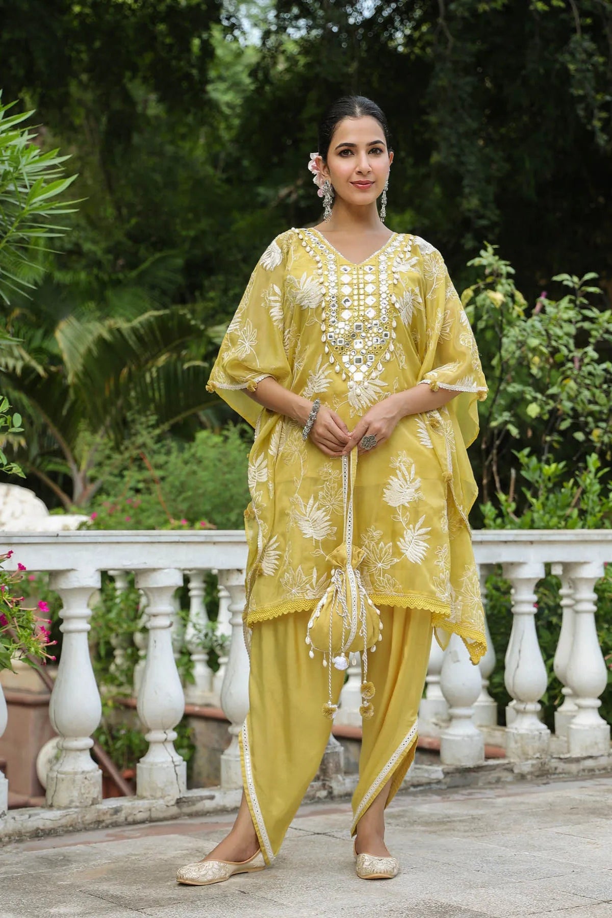 Woman in a yellow traditional outfit with white embroidery standing outdoors.
