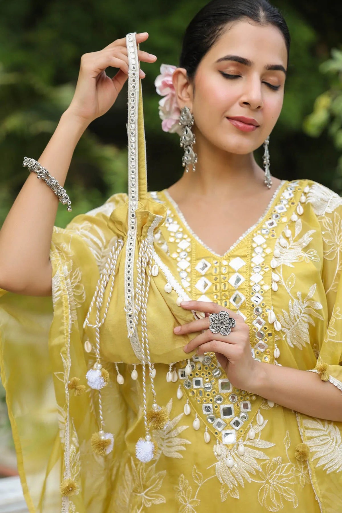 Woman in a yellow embroidered outfit holding jewelry outdoors